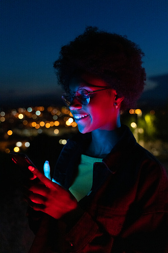Young woman using her mobile phone at night with the city at background