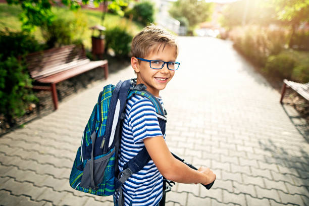 verticale d'un petit garçon conduisant à l'école sur le scooter de poussée - glasses child little boys happiness photos et images de collection