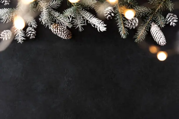 Photo of Happy New Year and Merry Christmas with sparkling garland on black stone table with gold bokeh background and pine branches. Holiday festive concept.