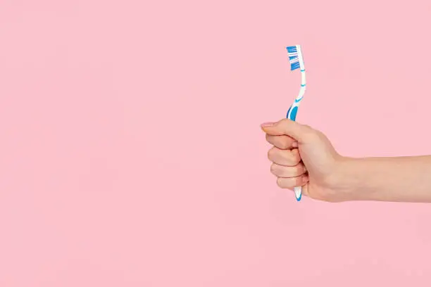 Crop female hand demonstrating blue toothbrush against pink backdrop