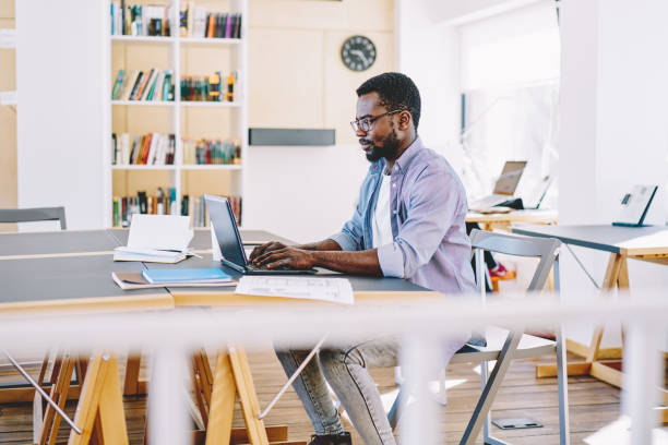 istock Professional dark skinned male freelancer typing on laptop computer sitting at desktop in coworking space, young african american guy making research while learning via online courses on netbook 1163539209