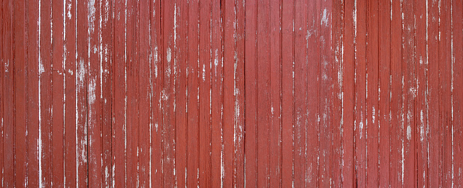 Panorama of a weathered red brown wooden wall made of vertical boards