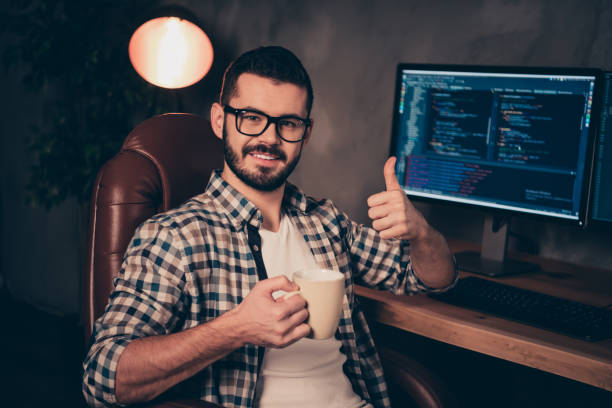istock Close up photo stubble handsome he him his guy support programming hands arms mug beverage thumb up coder code development outsource IT two monitors table office wear specs formalwear shirt 1163541732