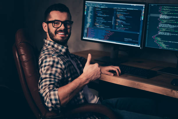 istock Close up side profile photo handsome he him his guy coder advising web agency thumb up keyboard development outsource IT processing language two monitors table office wear specs formalwear plaid shirt 1163542244