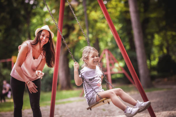 istock Happy mother swinging daughter at park 1163544109