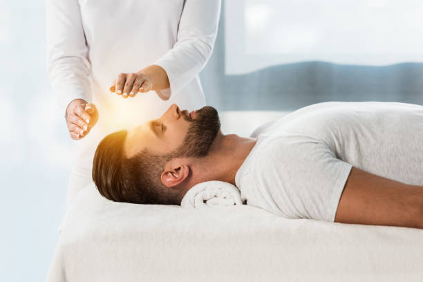 cropped view of healer putting hands above head of young man with closed eyes cropped view of healer putting hands above head of young man with closed eyes reiki photos stock pictures, royalty-free photos & images