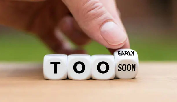 Hand flips a dice and changes the expression "too early" to "too soon" or vice versa.