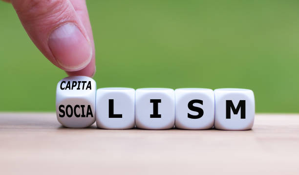 Hand flips a dice and changes the word "Socialism" to "Capitalism", or vice versa. Hand flips a dice and changes the word "Socialism" to "Capitalism", or vice versa. capitalism stock pictures, royalty-free photos & images