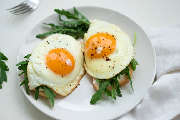 istock Sandwiches with ricotta cheese, arugula and fried egg on white wooden background. Selective focus. Healthy food concept 1163547475
