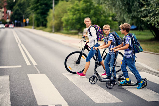 дети едут в школу на велосипеде и скутерах - teenager school walking education стоковые фото и изображения