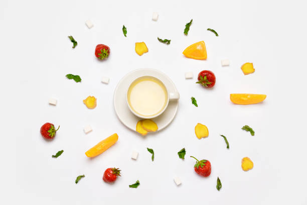 White cup of tea and fresh strawberries, pieces of ginger, orange, mint and sugar on a gray background. Flat lay, top view.