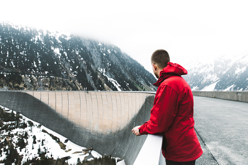 Young man in red jacket walking on the bid dam and enjoying the view of Austrian Alps