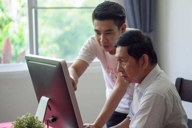 Grandson teaching grandfather how to Using computer and technology in home . young Teacher help senior Man learning to connect internet stock photo