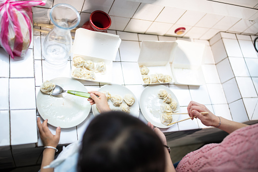 Woman and her adorable daughter working together in the kitchen, serving Chinese dumplings on plate