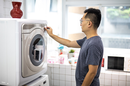 Mid adult Asian Man operating washing machine, pushing button