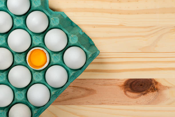 Many white chicken eggs in tray box. wood pinus background space for text background space for text. Egg broken in half.