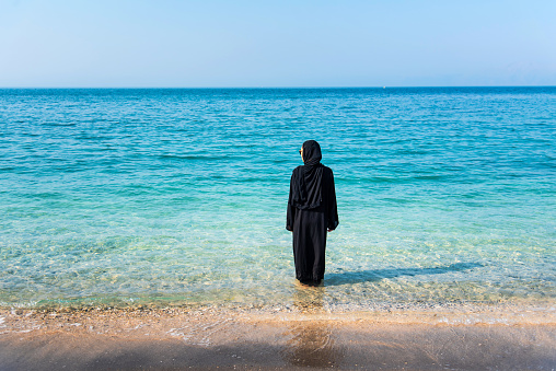 Muslim woman in abaya on the beach back view