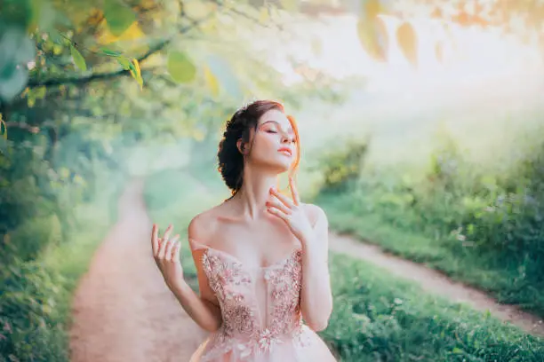 charming goddess of the spring forest stands on a narrow path and breathes in the sweet smell of nature, pleasure in motion, lady with her eyes closed strokes her beautiful neck with her fingertips.