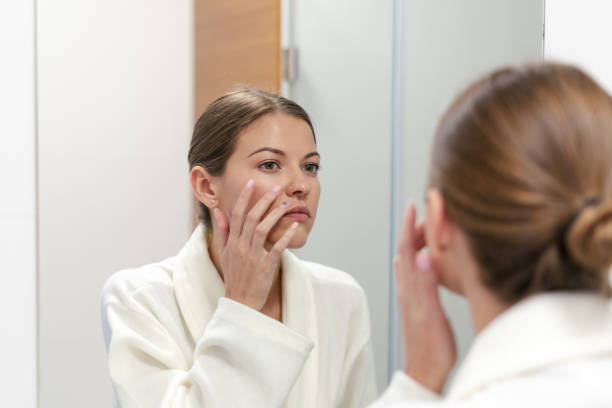 istock Woman in bathrobe looking in mirror at bathroom 1163569772