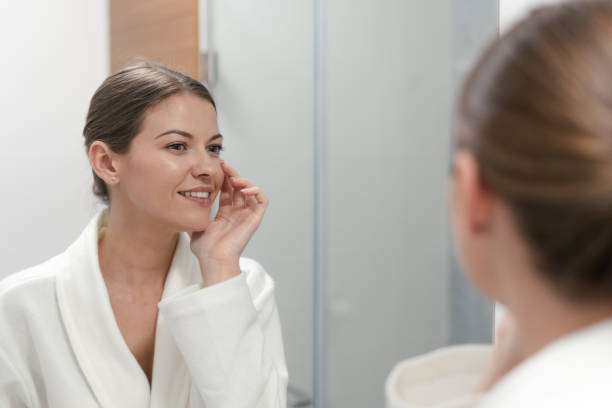 istock Woman in bathrobe looking in mirror at bathroom 1163569812