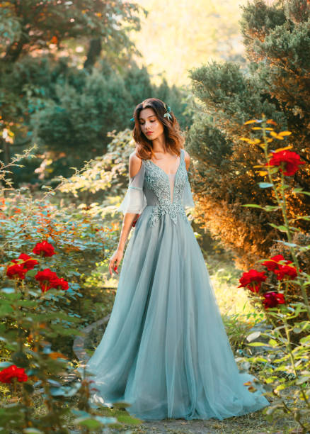 esbelta dama en claro vestido de verano turquesa con corte en el pecho y los hombros abiertos, princesa con el pelo oscuro mira príncipe en el parque, chica con sonrisa brillante, emociones positivas, retrato de arte de la modelo - evening gown fotografías e imágenes de stock