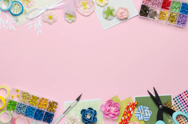 Paper flowers, tools, paper and scrapbooking items on pink background