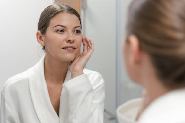 istock Woman in bathrobe looking in mirror at bathroom 1163569911