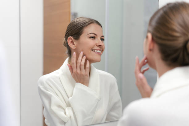 istock Woman in bathrobe looking in mirror at bathroom 1163569953