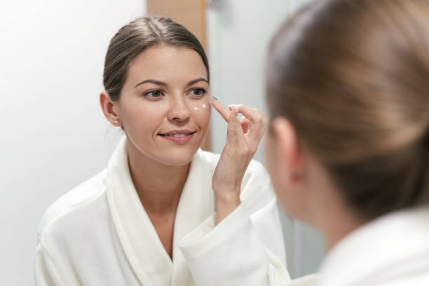 istock Woman standing in bathroom, applying cream on face 1163570060