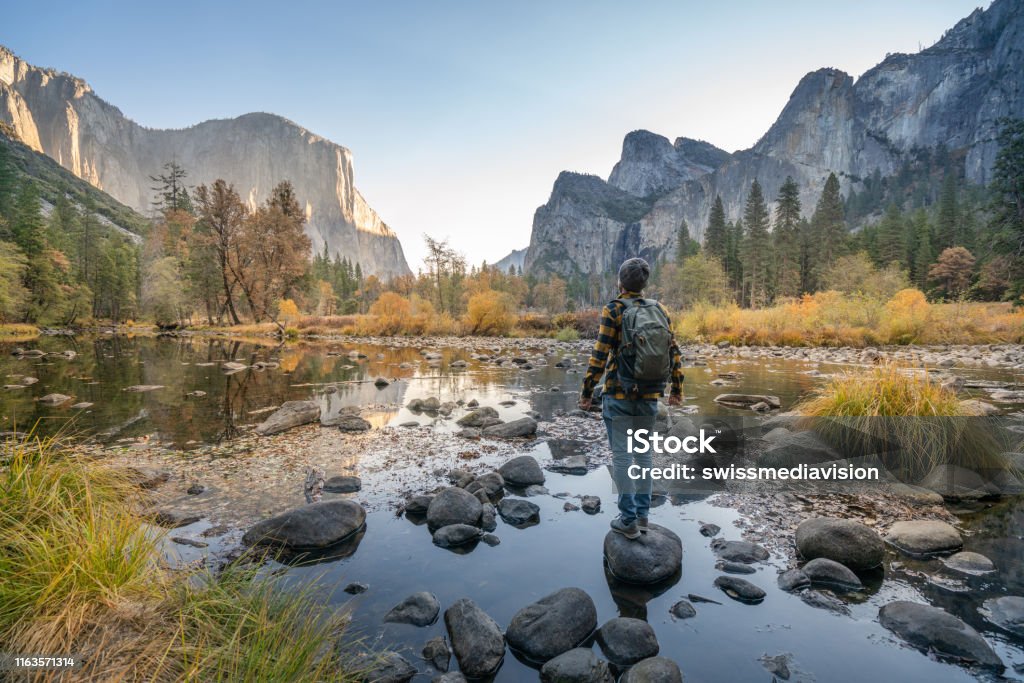 Young man contemplating Yosemite valley from the river, reflections on water surface Young man contemplating Yosemite valley from the river, USA Yosemite National Park Stock Photo