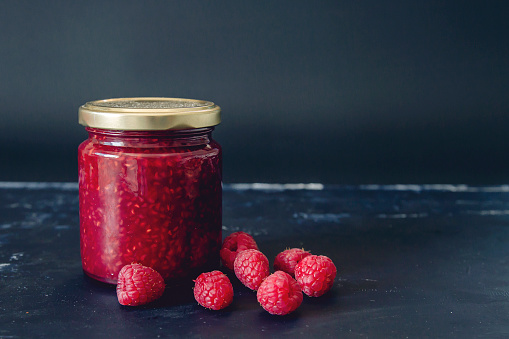 Swwet fresh homemade raspberries jam jar on dark background