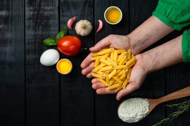 Model holding penne of pasta with eggs on black background. Ready for cooking