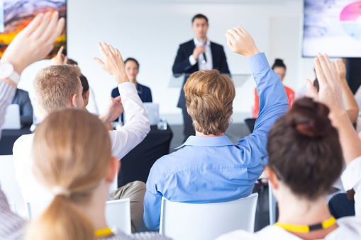 Rear view of audience raising their hands in a business conference . International diverse corporate business partnership concept