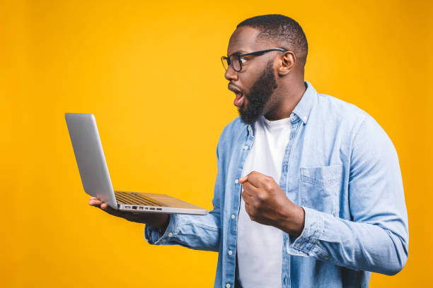 istock Young surprised african man standing and using laptop computer isolated over yellow background. 1163575454