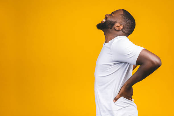 jeune jeune homme afro-américain souffrant de maux de dos pour avoir fait un effort sur le fond isolé. - human muscle back muscular build men photos et images de collection