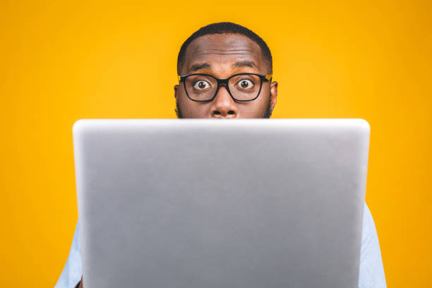 istock Young surprised african american man standing and using laptop computer isolated over yellow background. 1163576084