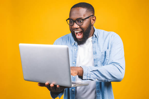 istock Young surprised african american man standing and using laptop computer isolated over yellow background. 1163576122