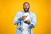 Portrait of a happy young afro american man throwing out money banknotes isolated over yellow background.