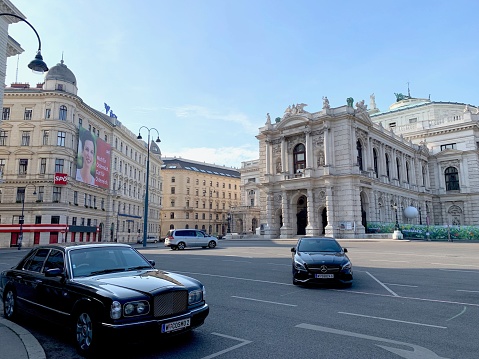 Vienna, Austria - July, 20 - 2019: Hofburg Theater, seen from the Café Landtmann on the left side. Two luxury cars parked in the foreground. On the left side the headquarters of the SPÖ party to be seen.