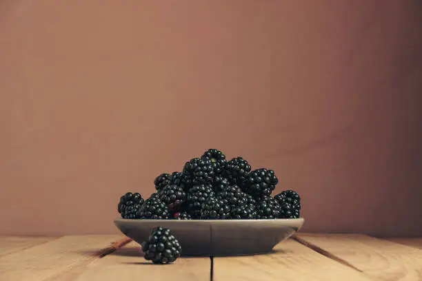 Fresh blackberry in bowl on a brown wooden table and dark-red wall background.