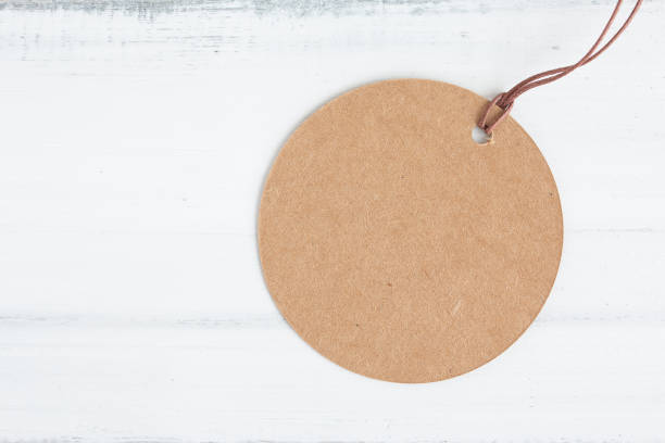 istock Brown round craft paper label on white wood table over white brick background with copy space. 1163579264