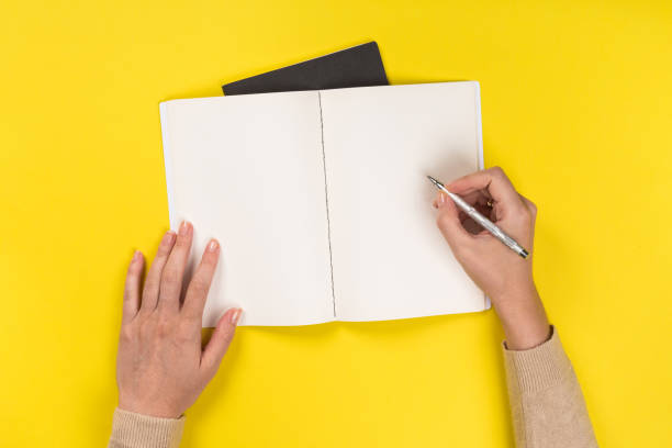 istock Woman's hands with perfect manicure holding pencil and  notepad as mockup for your design. Yellow background, flat lay 1163579743