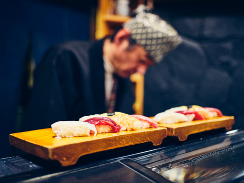 A Japanese sushi chef serving customers in a small sushi shop in Tokyo, Japan.