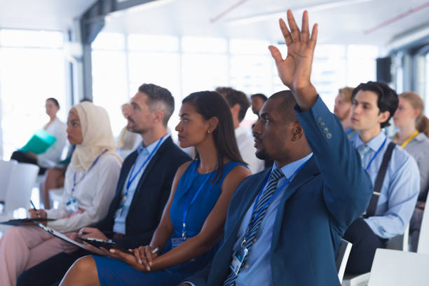 uomo d'affari alza la mano mentre partecipa a un seminario aziendale - attending foto e immagini stock