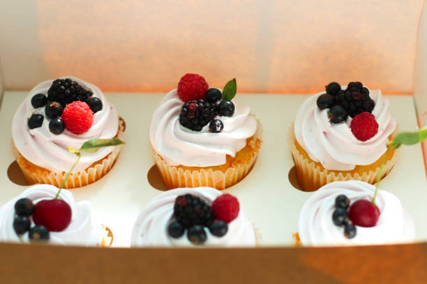 istock Isolated cupcakes with cream, cherry with a leaf, blackberry, raspberry black currant in a crafting box on a white background. 1163588433