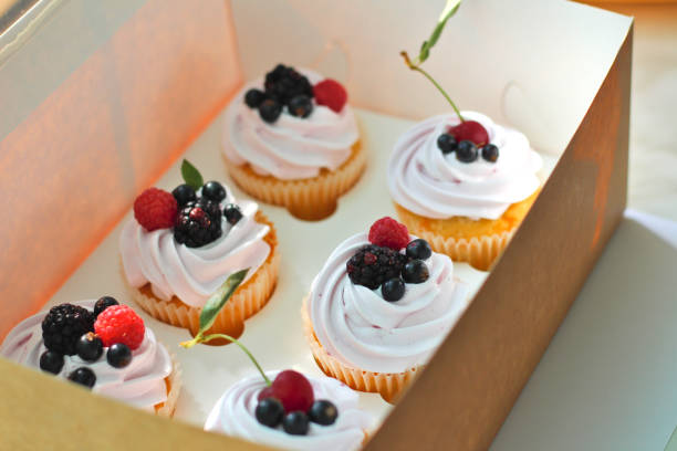 istock Isolated cupcakes with cream, cherry with a leaf, blackberry, raspberry black currant in a crafting box on a white background. 1163588435