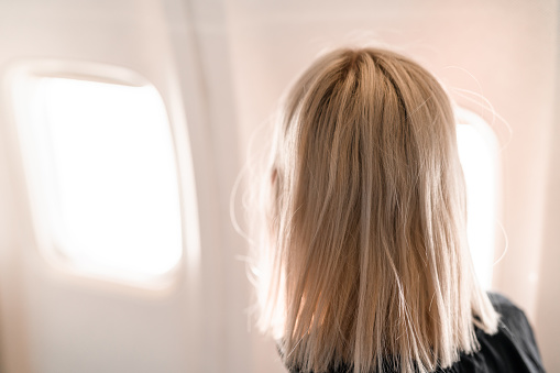 Young woman is traveling on an airplane. She is looking at the view through the window.