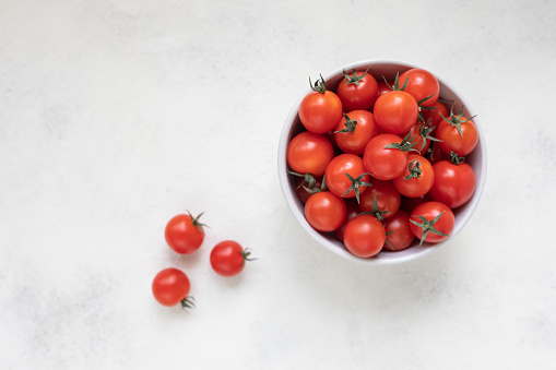 Cherry tomatoes in a bowl and on a white textural background, top view