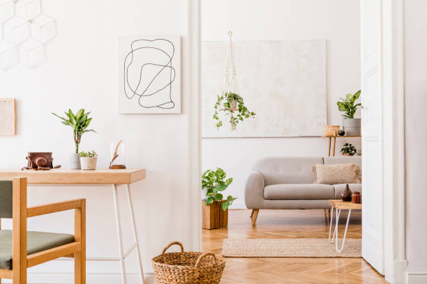 istock Boho open space interior in cozy apartment with design gray sofa, wooden desk and coffee table, plants and elegant personal accessories. Mock up poster frame on the white wall. Stylish home decor. 1163592099