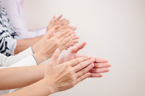 Close-up of group of business people clapping hands together while standing against the white background